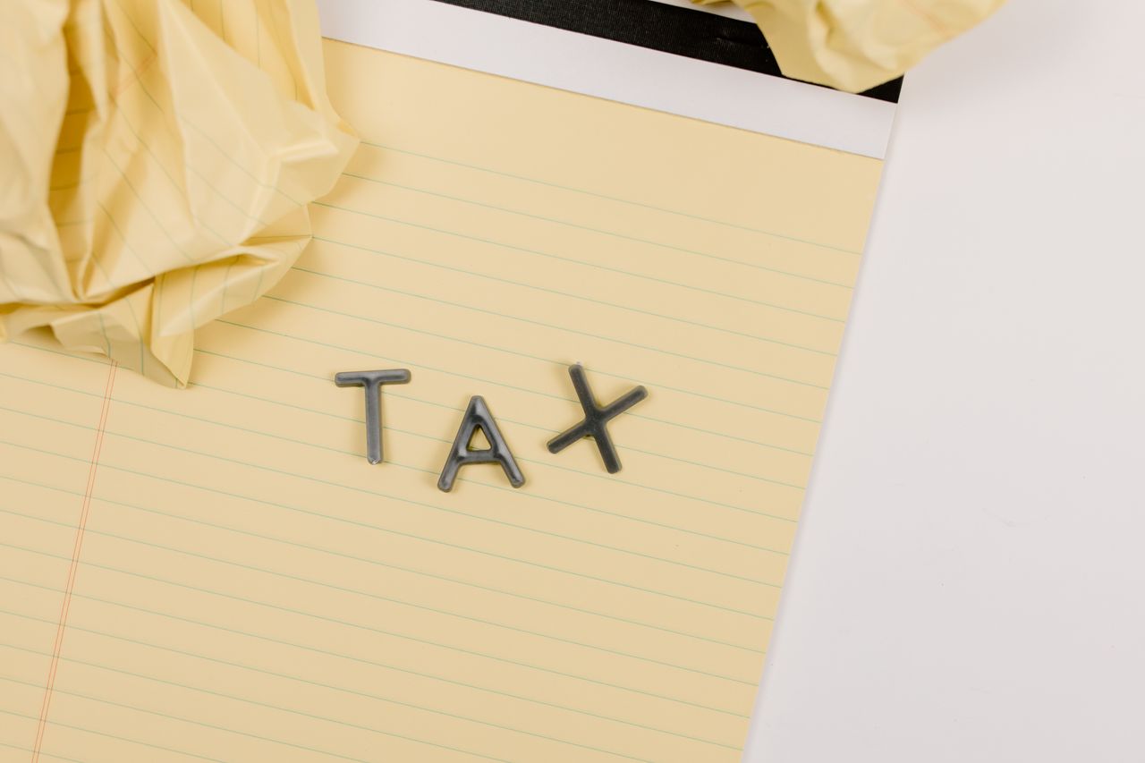 Close-up of a yellow lined paper with metal letters spelling 'tax', surrounded by crumpled paper.