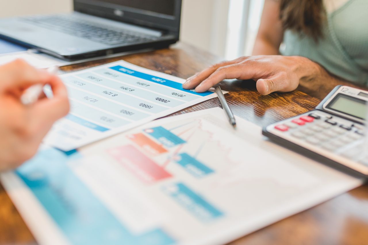 Hands at a desk with financial graphs, calculator, and pen, analyzing business data.